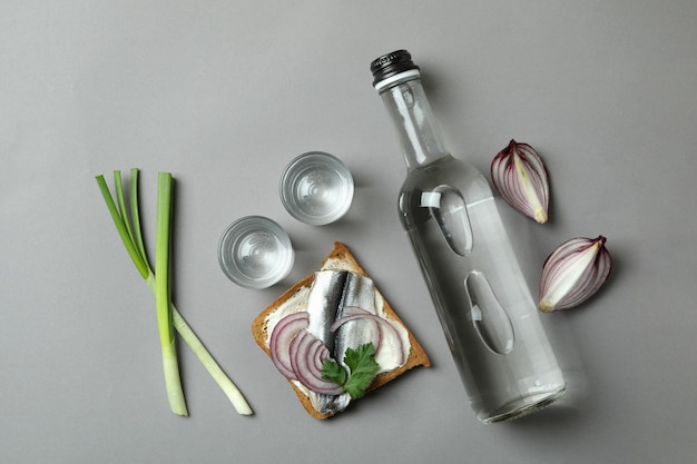 Botella y tragos de vodka y bocadillos sobre fondo gris