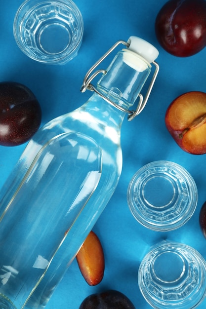 Botella y tragos de vodka de ciruela e ingredientes sobre fondo azul.