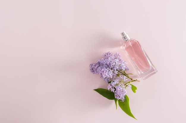 Una botella transparente de perfume de mujer sobre un fondo morado con una vista superior de flor lila un espacio de copia el concepto de publicidad de la fragancia