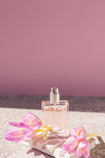 Foto una botella transparente de spray cosmético o perfume se encuentra en un podio en relieve blanco con flores de primavera presentación del producto vista frontal