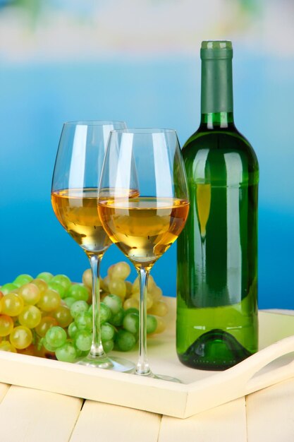 Botella de uvas maduras y copas de vino en bandeja sobre fondo brillante