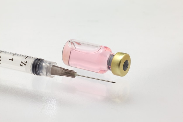Botella de vacuna de vidrio aislada acostada con líquido de color y jeringa maqueta de gran aumento muy cerca