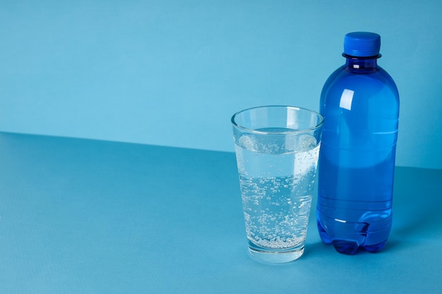 Botella y vaso de agua sobre fondo azul.