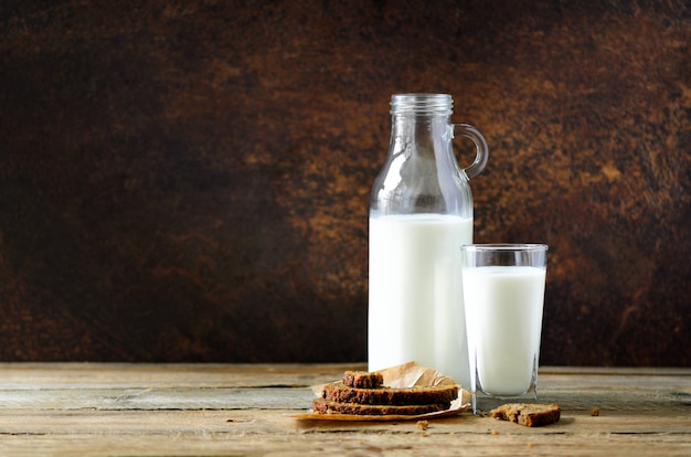 Foto botella y vaso de leche sobre fondo oscuro de madera.