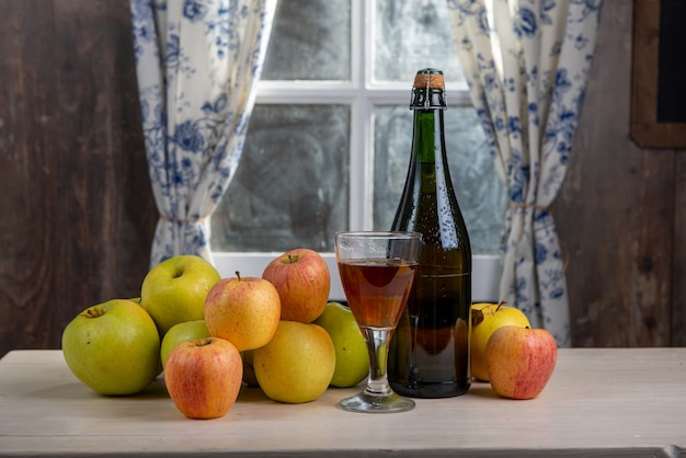 Botella y vaso de sidra con manzanas. En casa rústica