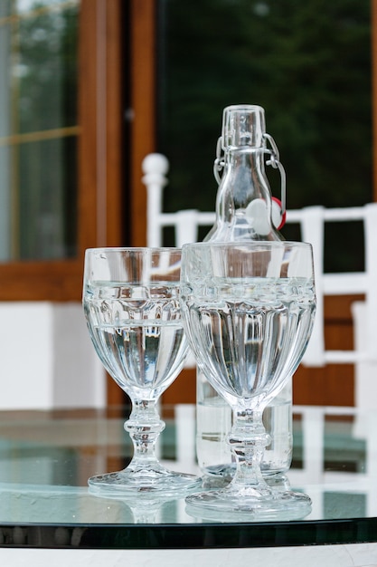 Botella y vasos de agua mineral en la mesa de vidrio en la terraza de la casa de campo