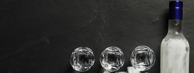 Botella de vasos de chupito de vodka y cubitos de hielo en la mesa negra plana con espacio para texto Diseño de pancarta