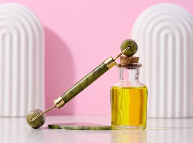 Botella de vidrio con aceite de masaje amarillo y masajeador de manos de piedra sobre medicina alternativa de fondo rosa