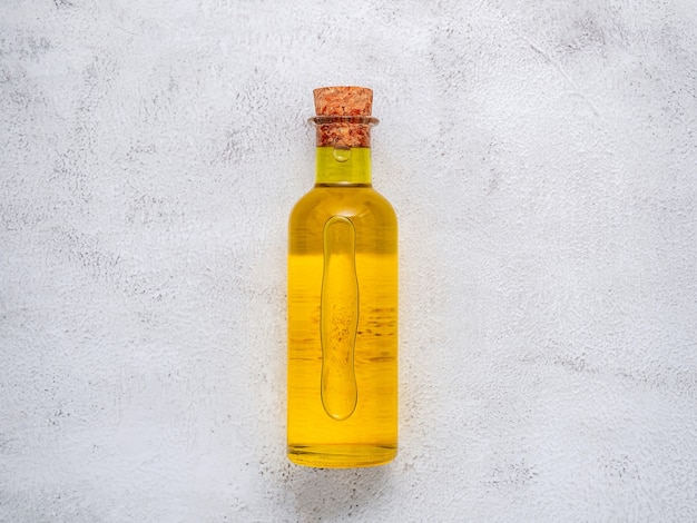 Foto botella de vidrio de aceite de oliva y rama de olivo sobre fondo de hormigón blanco.