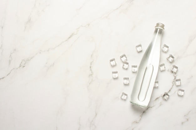 Botella de vidrio de agua y cubitos de hielo sobre una mesa de mármol.