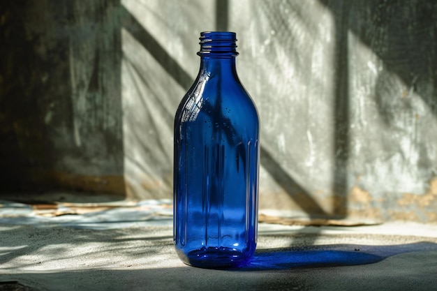 Botella de vidrio azul en la mesa con sombra en la pared y luz solar