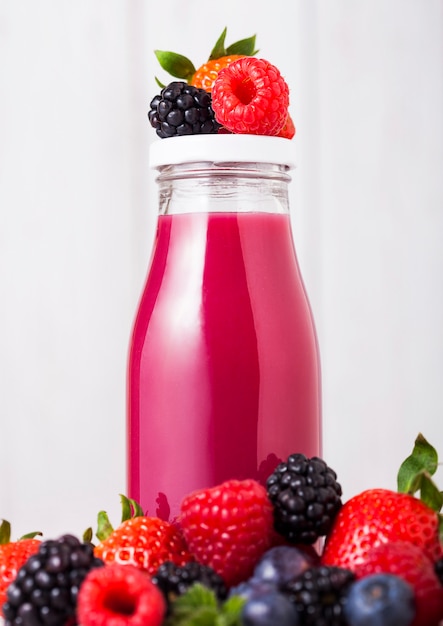 Botella de vidrio con batido de bayas frescas de verano en mesa de madera. Fresas y frambuesas con arándanos y moras.