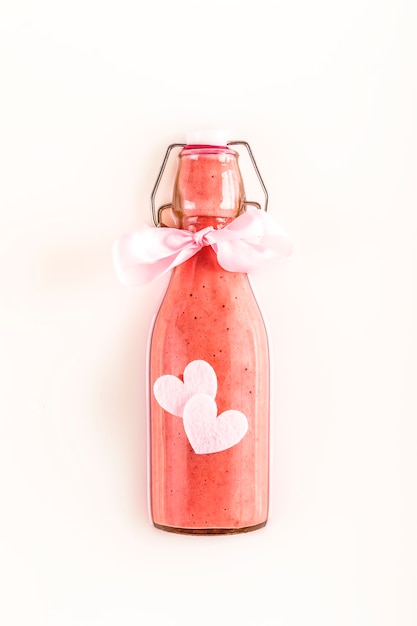 Foto botella de vidrio con batido de fresa rosa refrescante sobre leche con corazones encantadores. concepto de comida sana, detox y dietética. regalo.