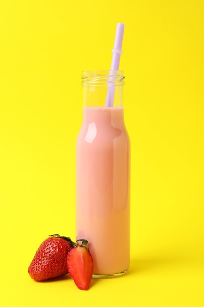 Botella de vidrio de batido de fresa sobre fondo amarillo