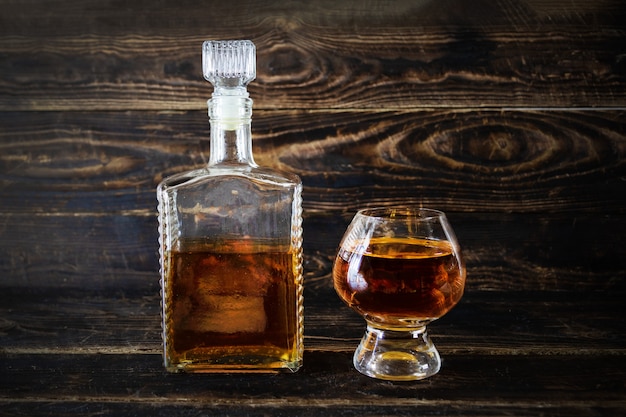 Botella de vidrio y copa de vino con coñac en la superficie de la tabla de madera, primer plano.