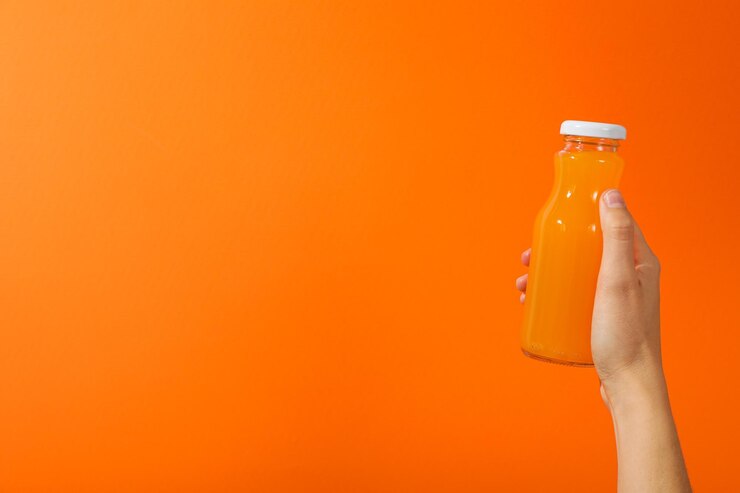 Botella de vidrio con jugo en la mano sobre fondo naranja espacio para texto