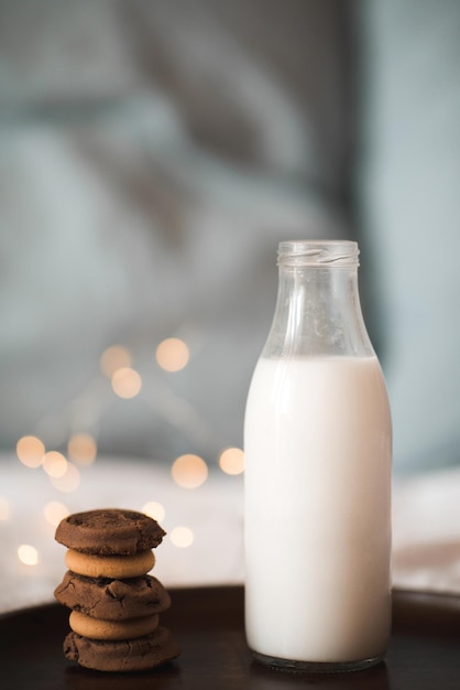 Botella de vidrio con leche fresca y pila de galletas de chocolate en bandeja de madera en primer plano de la cama. Desayuno sabroso. Buenos días. Estilo de vida de nutrición saludable.