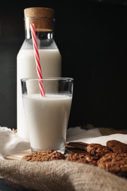 Botella de vidrio de leche y galletas sobre fondo oscuro