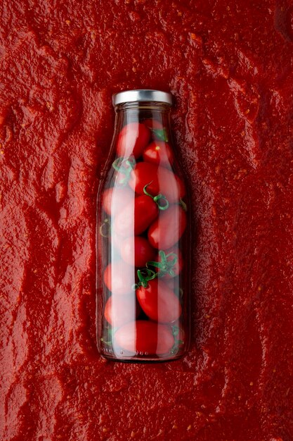 Botella de vidrio llena de tomates reposando sobre una base de salsa de tomate