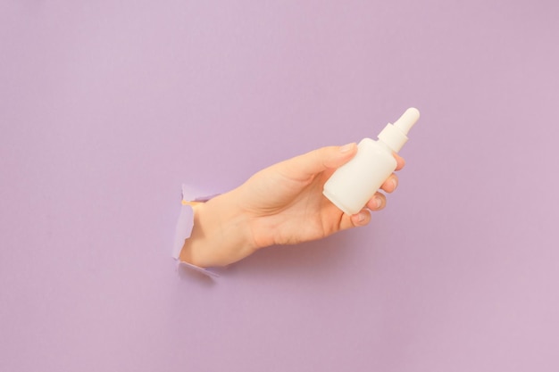Foto botella de vidrio para la mano con tapa de gotero contenedor blanco con aceite esencial de suero de productos cosméticos sobre fondo lila concepto de belleza
