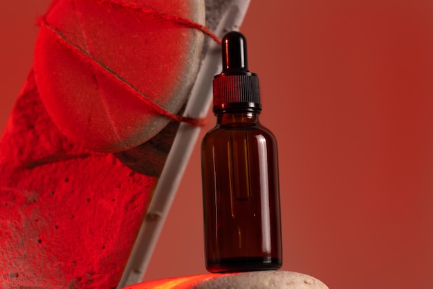 Botella de vidrio marrón de producto cosmético o aceite sobre piedra en fondo de luz roja Concepto de belleza cosmética futurista belleza moderna