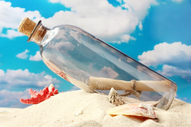 Botella de vidrio con una nota en el interior en arena sobre fondo de cielo azul