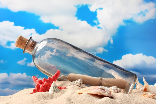 Botella de vidrio con una nota en el interior en arena sobre fondo de cielo azul