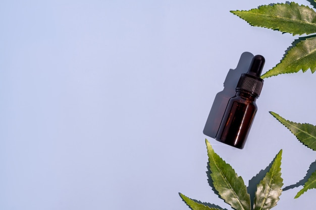 Botella de vidrio oscuro con aceite de CBD a base de hierbas, tintura y hojas de cáñamo sobre fondo azul claro. Aceite de cbd de cosméticos. Aceites esenciales naturales para rostro y cuerpo.