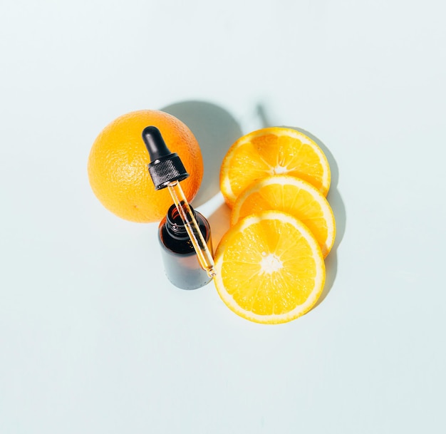 Botella de vidrio con productos cosméticos gel suero aceite anticelulítico producto de jugosa naranja madura sobre un fondo azul de sombras duras y soleadas