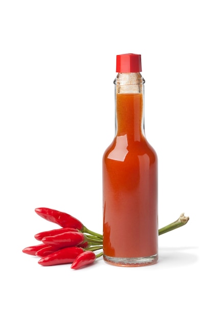 Botella de vidrio con salsa de chile picante y pimientos tabasco frescos aislados en fondo blanco de cerca