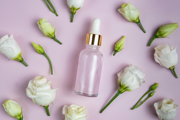 Una botella de vidrio transparente con colágeno o ácido hialurónico sobre un fondo rosa con flores dispersas de eustoma Lugar para el texto Suero para el cuidado cosmético de la piel cuidado suave