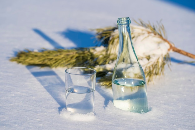 Botella de vidrio y vaso de agua sobre una nieve blanca en invierno