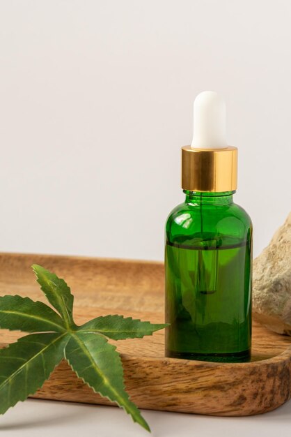 botella de vidrio verde con aceite de CBD tintura de THC y hojas de cáñamo sobre un fondo blanco estilo minimalismo cosméticos orgánicos cosméticos con aceite de THC