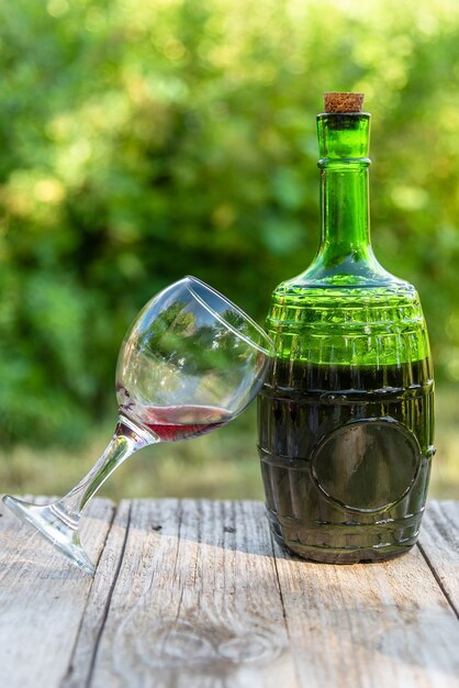 Botella de vidrio con vino tinto y una copa. al aire libre.