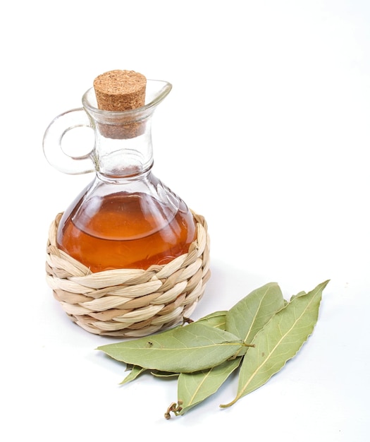 Botella de vinagre y hoja de laurel en el blanco.