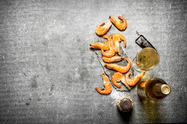 Botella de vino blanco con camarones en mesa de piedra.