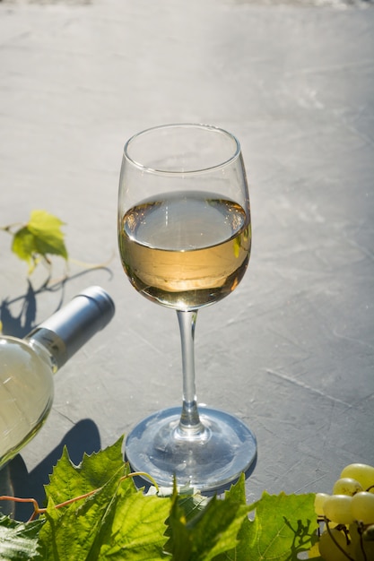 Botella de vino blanco con copa de vino, uva madura en mesa de hormigón gris.