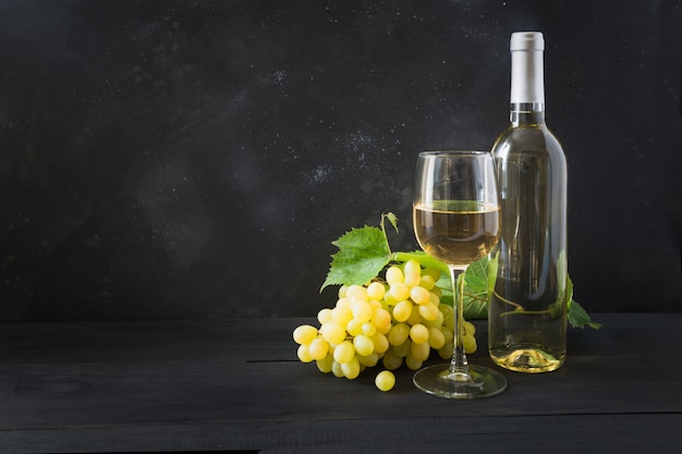 Botella de vino blanco con copa de vino, uva madura en mesa de madera negra. Copia espacio