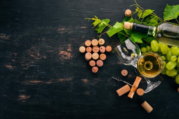 Una botella de vino blanco con copas y uvas Hojas de uva Vista superior Sobre un fondo de madera negra Espacio libre para texto