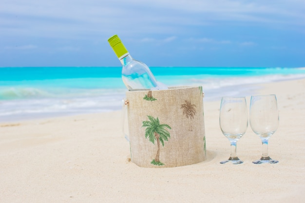 Botella de vino blanco y dos copas en la exótica playa de arena