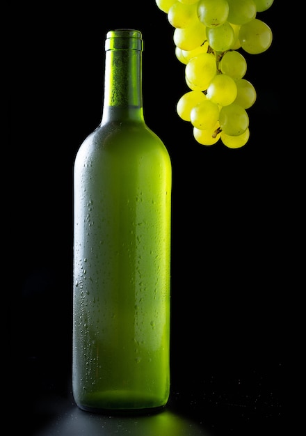 Botella de vino blanco muy fría con racimo de uvas blancas sobre negro