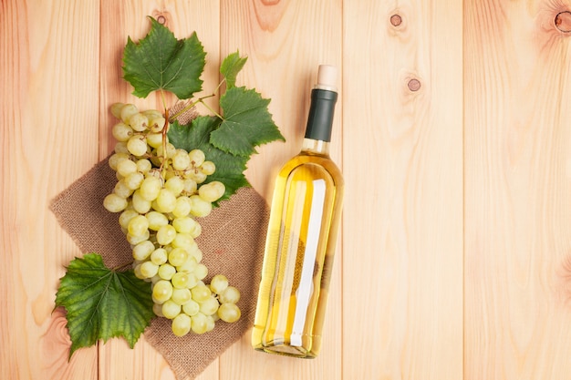 Botella de vino blanco y racimo de uvas blancas sobre fondo de mesa de madera con espacio de copia