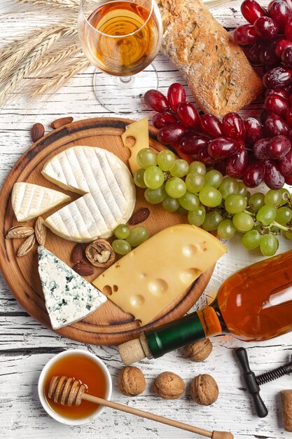 Botella de vino blanco, uva, miel, queso y copa de vino sobre tabla de madera blanca. Vista superior con espacio de copia.