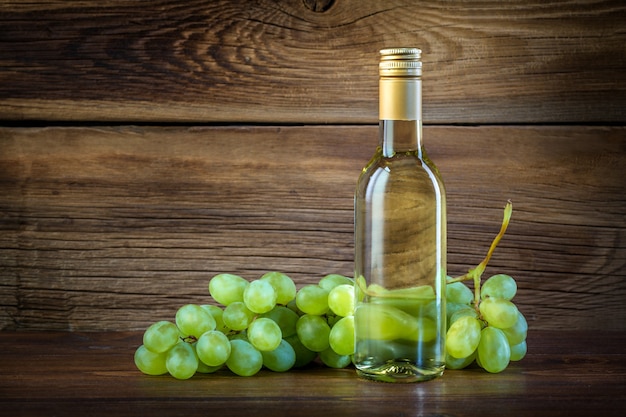 Una botella de vino blanco con uvas sobre un fondo de madera