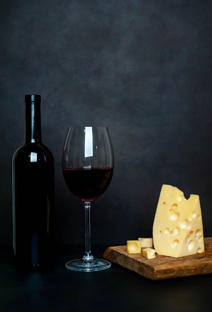 Botella de vino, copa de vino y sabroso queso en una tabla de cortar, piedra de fondo