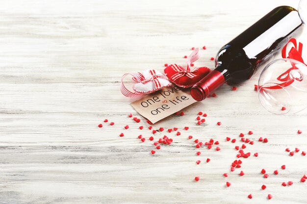 Botella de vino y copas con corazones hechos a mano sobre fondo blanco de madera - Concepto de San Valentín