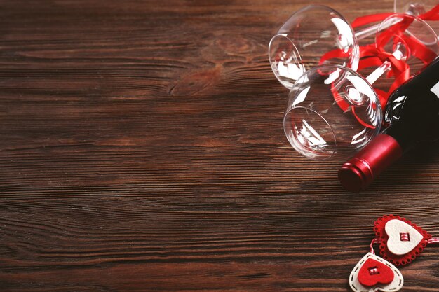 Botella de vino y copas con corazones hechos a mano sobre fondo de madera