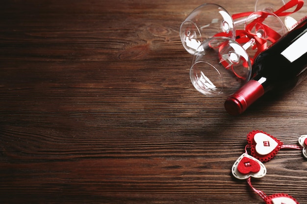 Botella de vino y copas con corazones hechos a mano sobre fondo de madera