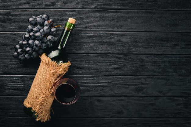 Una botella de vino con copas y uvas sobre un fondo de madera negra Espacio libre para texto Vista superior