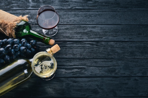 Una botella de vino con copas y uvas sobre un fondo de madera negra Espacio libre para texto Vista superior